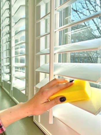 hand using the yellow duster to clean window blinds