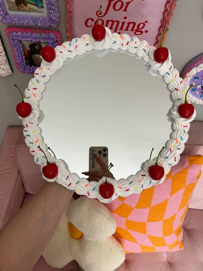 Person holding a whimsically decorated mirror with cherry and sprinkle edges 