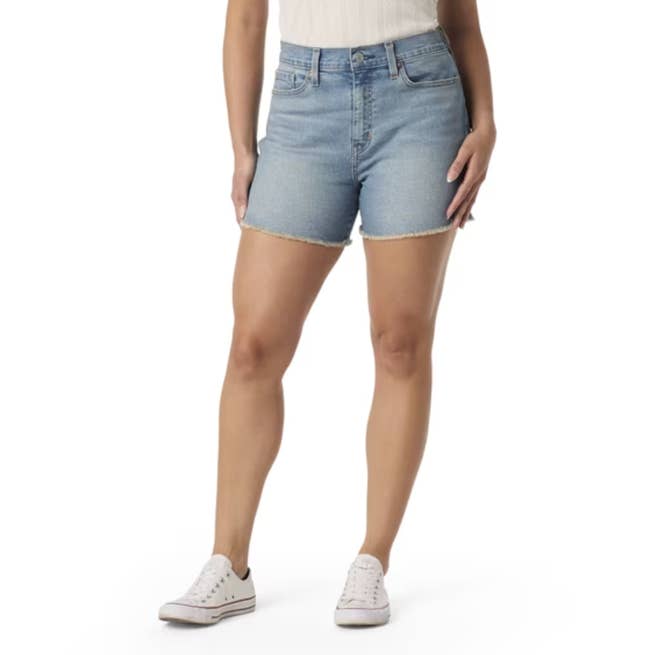 Person wearing denim shorts and achromatic sneakers, lasting with hands by their sides