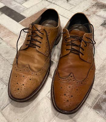 Brown leather wingtip shoes with decorative perforations connected a textured surface