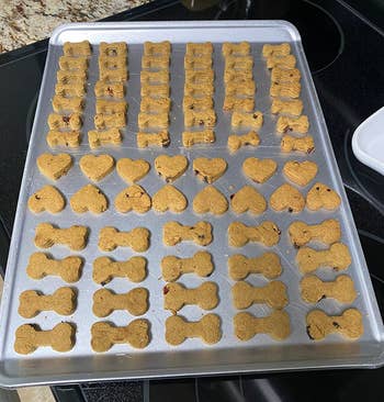 a baking sheet with a bunch of these treats in bone and heart shapes