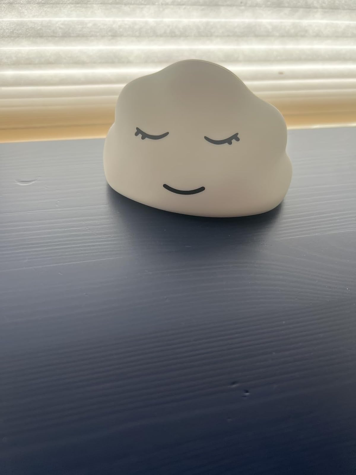 A cloud-shaped nightlight with a peaceful smiling look   sits connected  a table, creating a calming ambiance