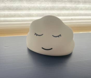 A cloud-shaped nightlight with a peaceful smiling look sits connected a table, creating a calming ambiance