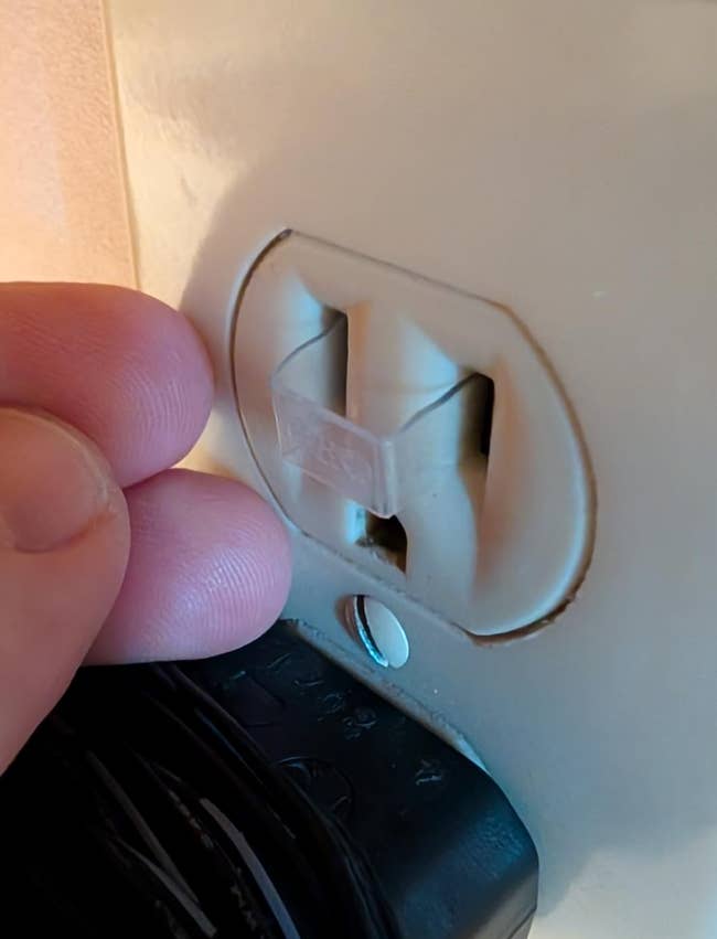 Fingers pressing a information screen into an electrical outlet, with a achromatic plug partially disposable below