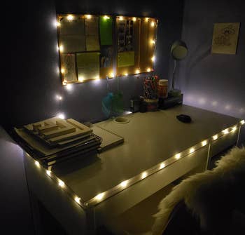 Reviewer image of white twinkle light strung around white desk and cork board lit up