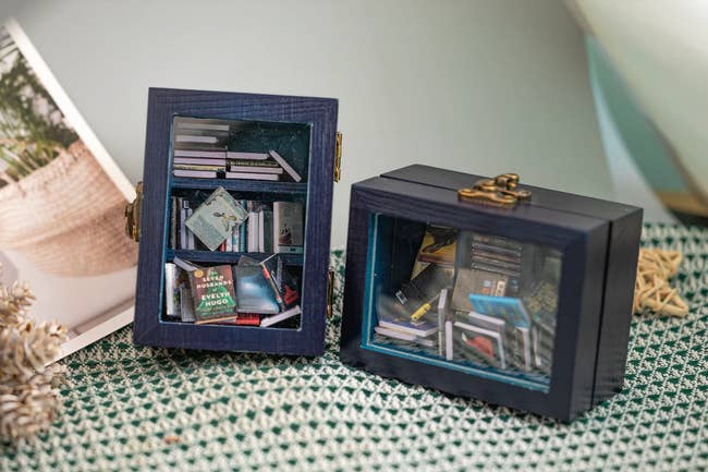 Two woody  hinged boxes with solid  windows and miniature books inside