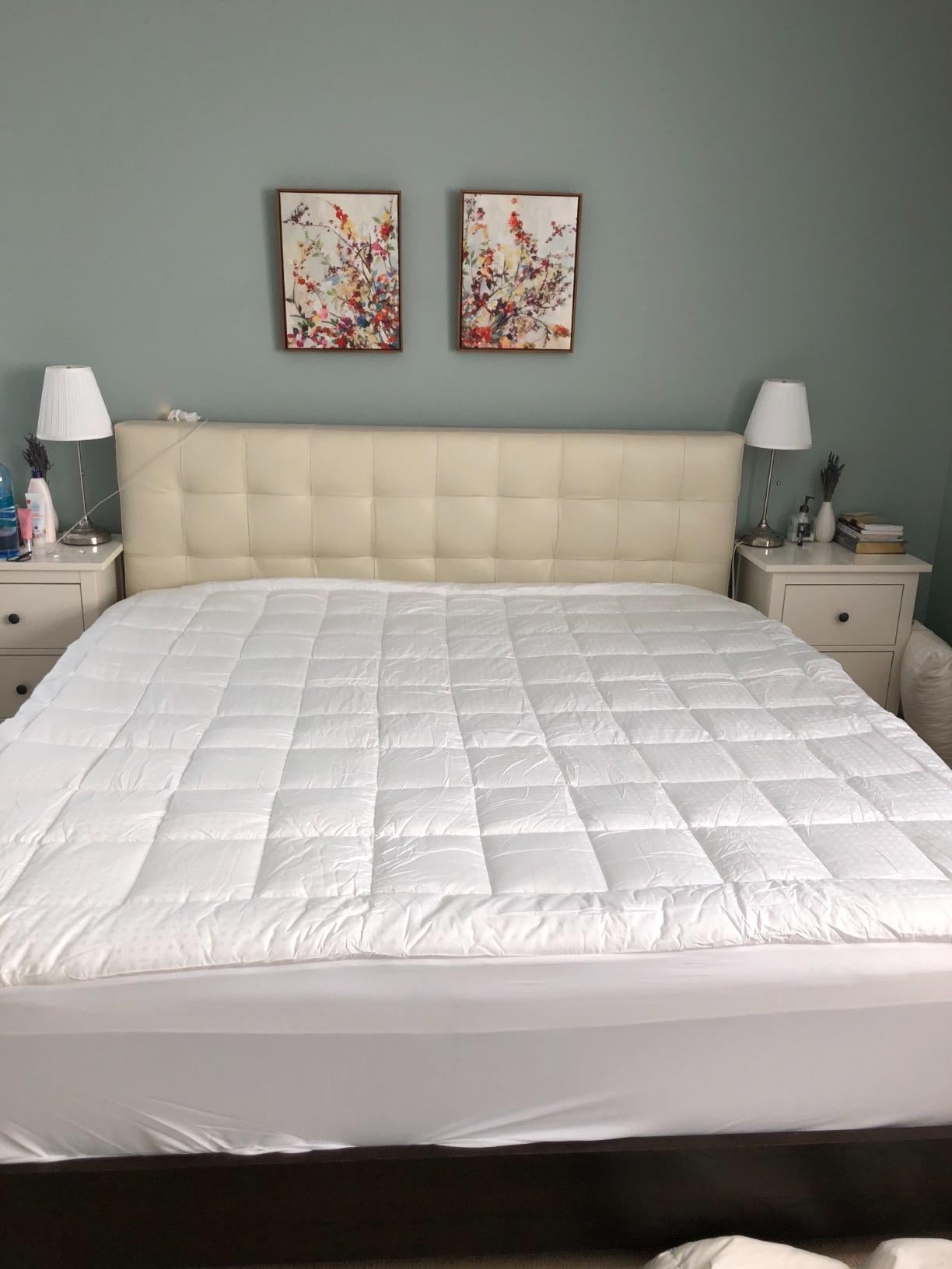 reviewer photo of the white quilted mattress cover on their unmade bed