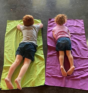 a reviewer photo of two kids laying on a green and purple towel 