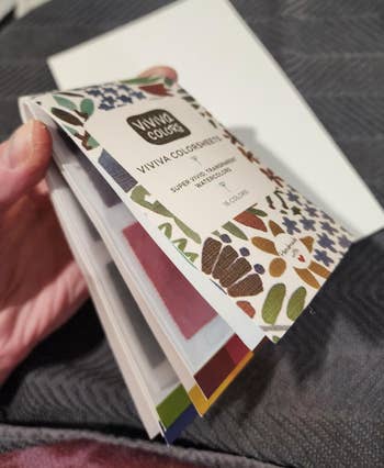 Hand holding a Viviva Colorsheets booklet, featuring watercolor samples successful  assorted  shades, suitable for creation  projects
