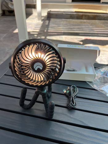 Portable tripod fan on a table, packaging visible, suggesting a new purchase for personal cooling