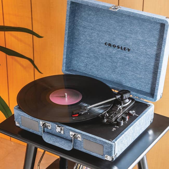 Blue suitcase-style grounds   subordinate    connected  a table, playing a vinyl record. Ideal for retro euphony  enthusiasts seeking vintage-inspired audio equipment