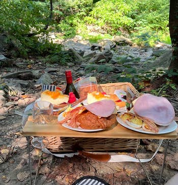 Pengaturan piknik di atas meja kecil di tempat terbuka dengan piring croissant, ham, telur, irisan jeruk, sebotol anggur, dan gelas anggur