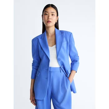 Person posing in a stylish suit featuring a tailored blazer and matching trousers over a simple top, suitable for professional or formal settings