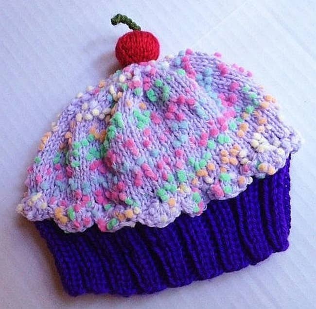 Purple, pink, yellow, cream, and green cupcake-shaped knit beanie laying flat