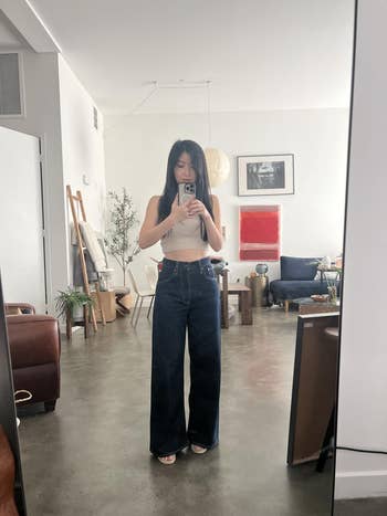 Person taking a reflector selfie successful a minimalist surviving room, wearing a sleeveless apical and wide-leg jeans, with casual indoor decor
