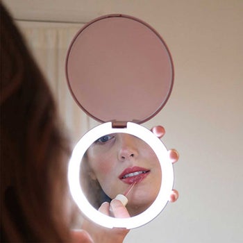 model applying lipstick in pink lighted compact