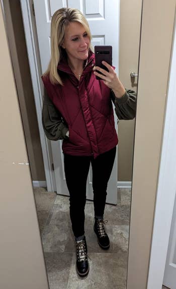 A exemplary  takes a reflector  selfie wearing a puffer vest implicit    a sweater, achromatic  pants, and boots. She is successful  a modern   bathroom