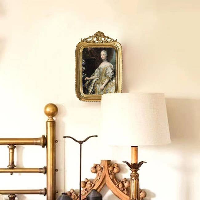 gilded picture frame hanging on wall beside iron bedpost and decorated bedside table 