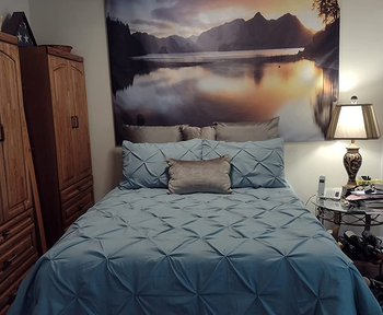 Reviewer image of teal pleated full-size comforter set with matching shams made up on a bed next to wooden closet