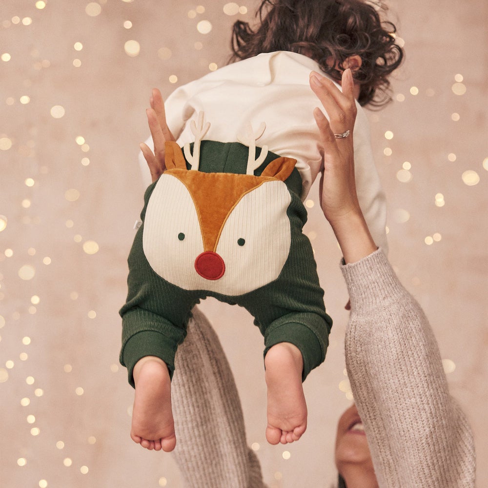 a baby wearing green pants with a reindeer on the butt