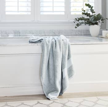 a light blue plush bath towel hanging on the edge of a tub