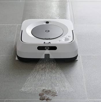 The iRobot vacuum spraying a cleaner on a floor covered in muddy prints
