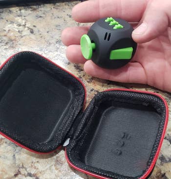 Reviewer image of black and green fidget cube with red and black case