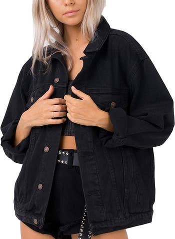 A person is wearing an black oversized denim jacket over a cropped top and high-waisted shorts with a belt
