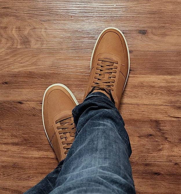 Person wearing casual brown sneakers and blue jeans, standing on a wooden floor