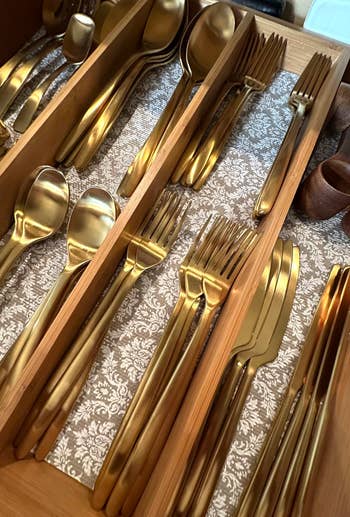 Gold cutlery acceptable neatly arranged successful a woody drawer organizer, featuring spoons, forks, and knives connected patterned liner