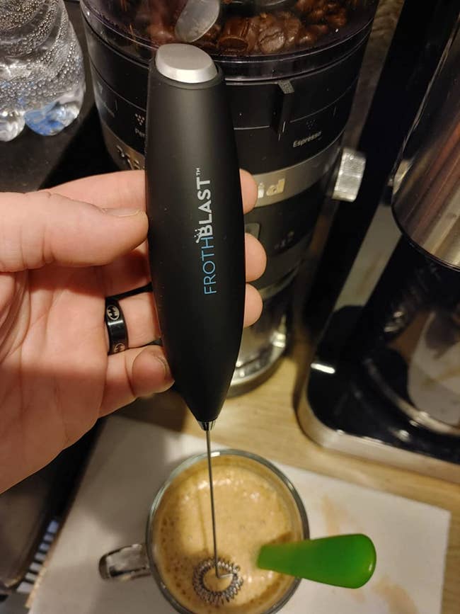 Reviewer holding black milk frother above glass of coffee 