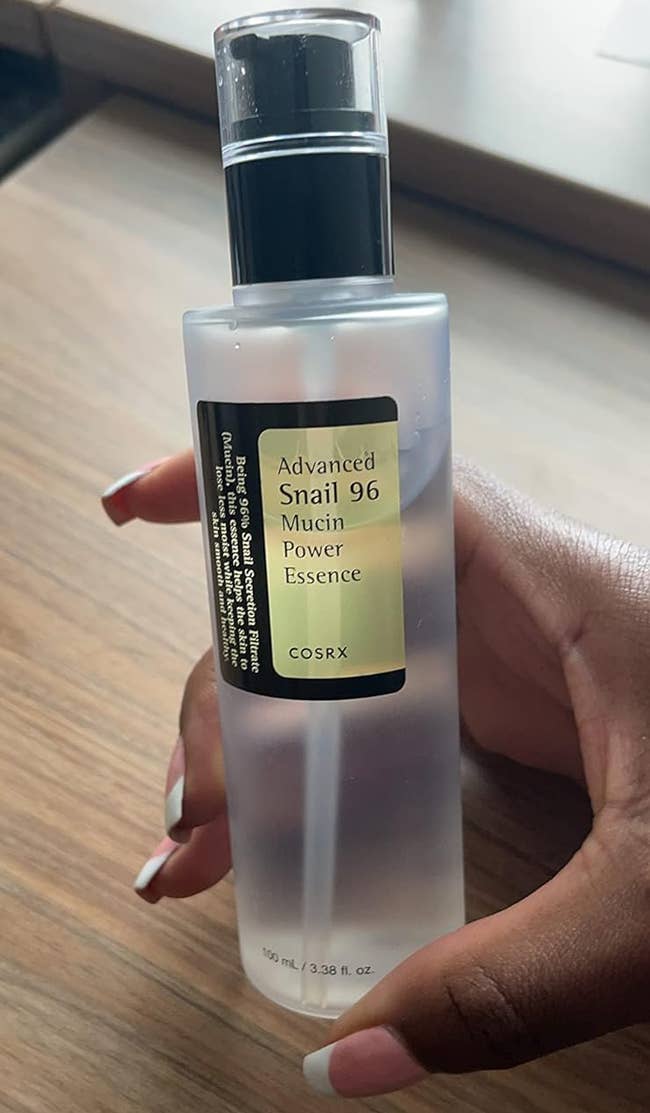 A hand holding a bottle of COSRX Advanced Snail 96 Mucin Power Essence
