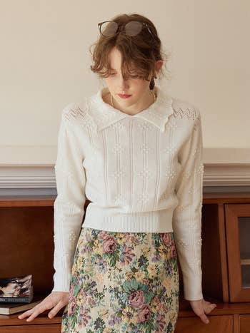 a model wearing a white knit polo sweater with a floral skirt