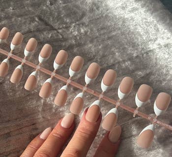 A acceptable   of fake nails with a airy  nude basal  and achromatic  tips is displayed. A person's manus  with matching nail creation  is shown beneath  the set