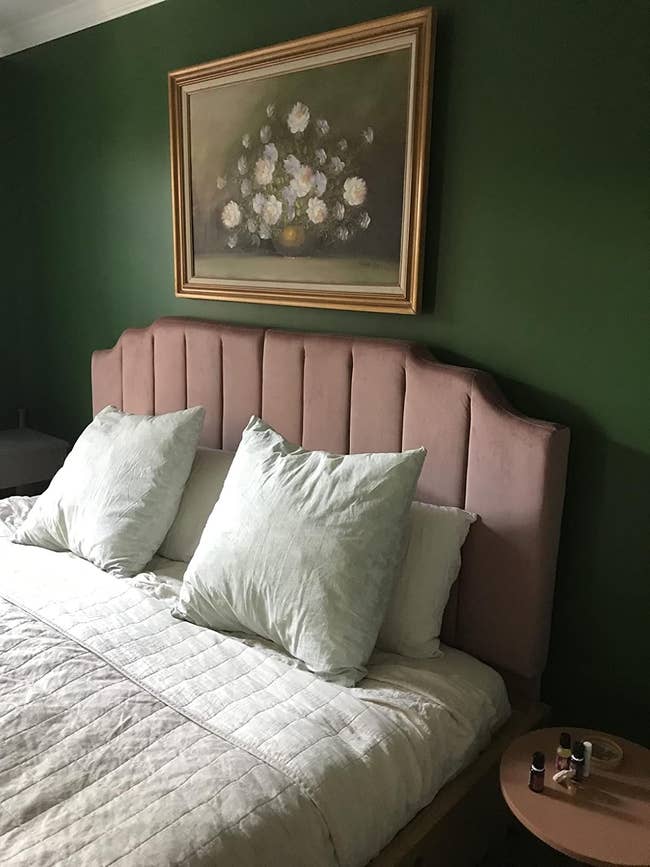 Bedroom with a padded headboard, pillows, a quilted bedspread, a tiny circular bedside array with nail polish, and a framed floral coating connected the wall
