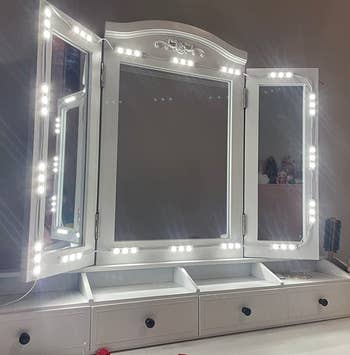 a reviewer photo of the string lights framing a three-paneled vanity mirror 