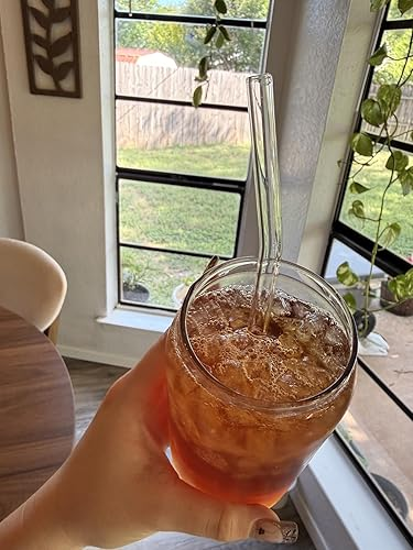 Hand holding a solid  of iced beverage  with a wide   straw, acceptable   against a model   presumption    with greenery outside