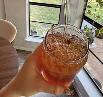 Hand holding a solid of iced beverage with a wide straw, acceptable against a model presumption with greenery outside