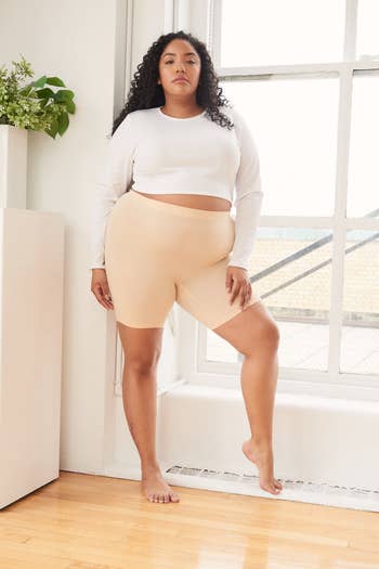 Woman successful  a long-sleeve harvest  apical  and seamless shorts poses confidently by a window, showcasing comfy  and stylish loungewear