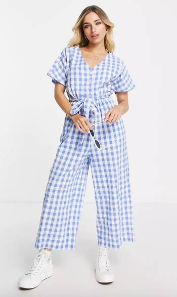 model wearing the blue and white gingham jumpsuit with white sneakers