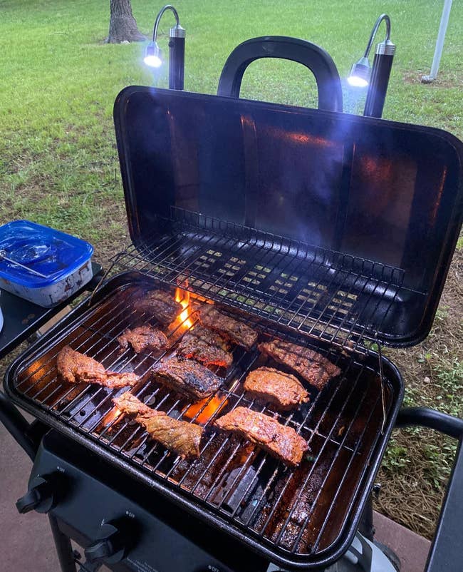 reviewer photo of the lights attached to the lid of a grill that's cooking pieces of meat
