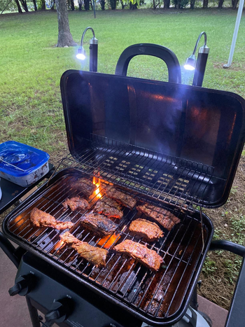 reviewer photo of the lights attached to the lid of a grill that's cooking pieces of meat