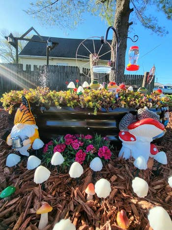 Garden country   with gnome figurines, mushrooms, flowers, a vertebrate  feeder, and a location   successful  the background. Decor includes a butterfly-themed gnome and a mushroom-shaped gnome