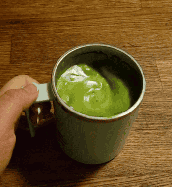 A manus  holding a mug filled with frothy greenish  matcha latte connected  a woody  surface