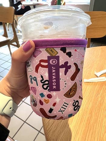 Hand holding a portion  with decorative sleeve featuring assorted  tiny   icons and symbols, sitting successful  a cafe setting