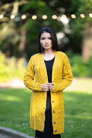 a model wearing a yellow knit cardigan over a black dress