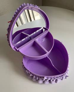 The inside of the lavender heart-shaped jewelry box, showing two larger containers for storage on the bottom, two smaller storage containers on top, and a mirror