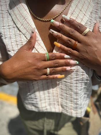 Close-up of hands with originative nail creation holding a checkered-patterned blazer. Several rings adorn the fingers, adding a fashion-forward touch