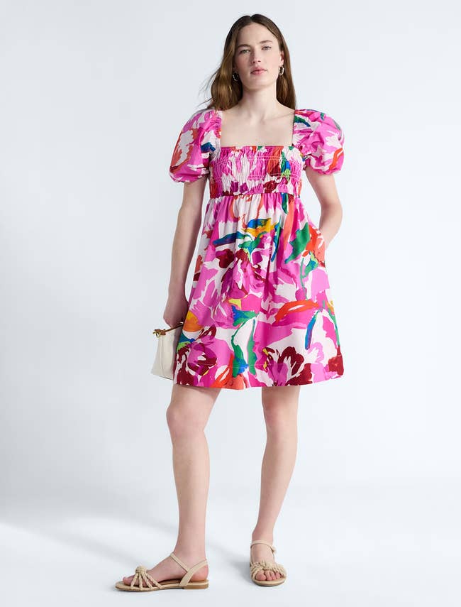 Person wearing a floral people formal with puff sleeves, holding a tiny bag, and wearing sandals
