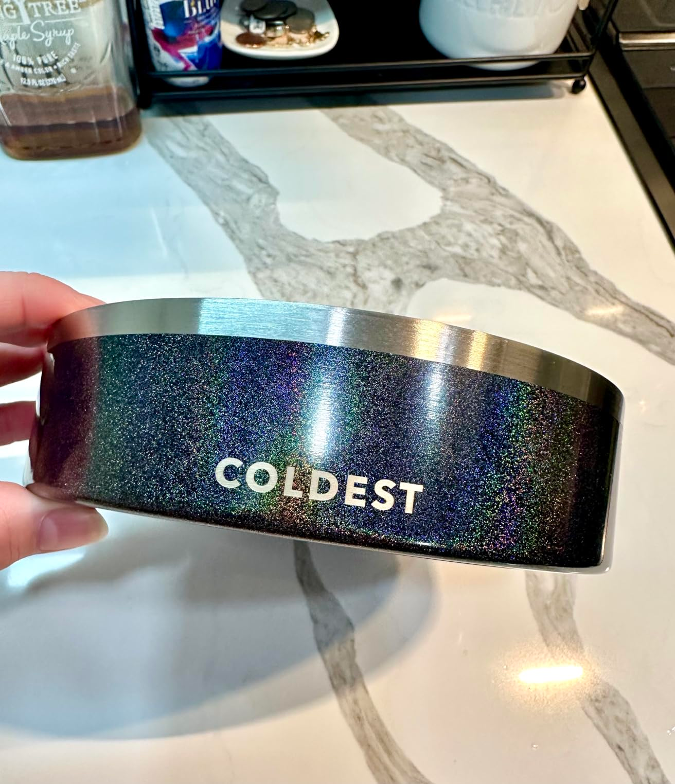 A hand holds a black, sparkling insulated cup labeled